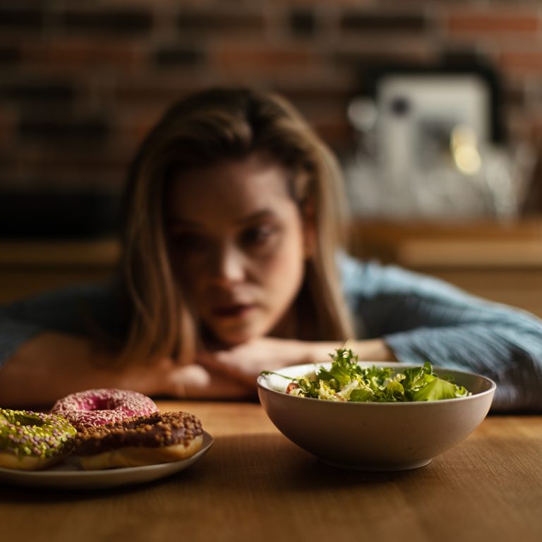 Young woman having diet, deciding between a salad and donuts.