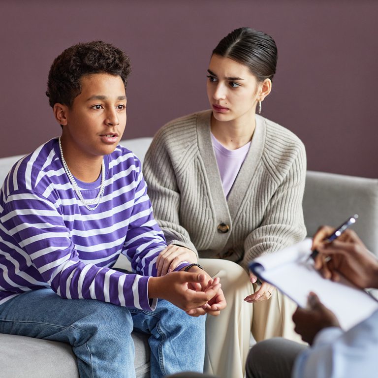 Worried young woman looking at teenage son telling psychologist about his problems in school