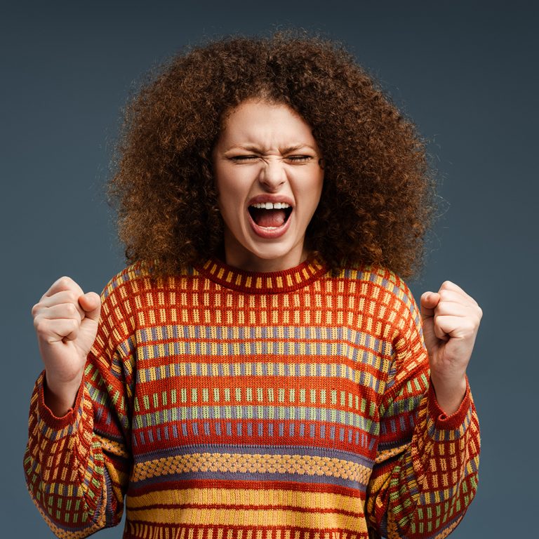 Upset, unhappy woman with curly hair with closed eyes screaming, standing isolated on gray background. Concept of emotional overload